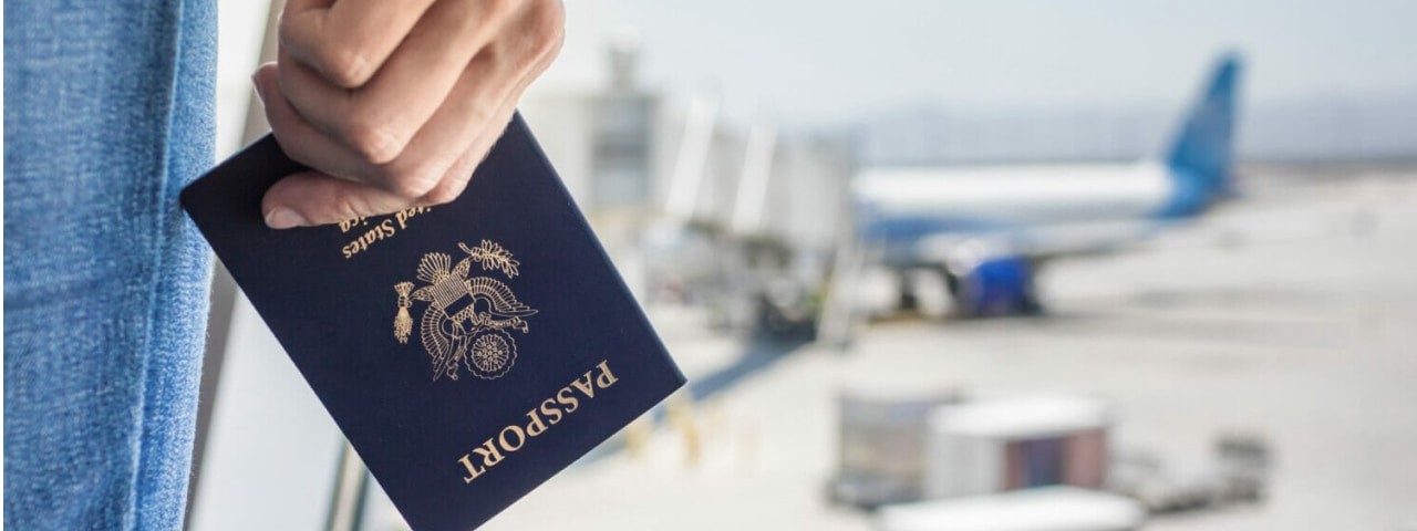 Closeup of a hand holding a passport at an airport with an airplane and luggage in the background